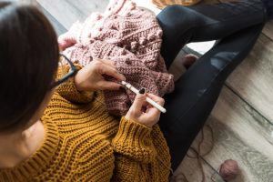 Dark-haired woman in a mustard yellow sweater working on a crochet project