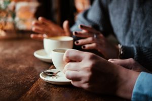 Two people sitting at a table talking with coffee cups in front of them