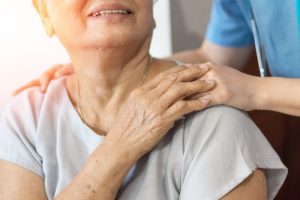 older woman holding a nurse's hand on her shoulder
