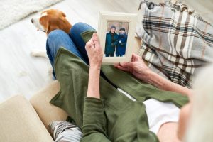 Woman in green cardigan sitting on couch as she holds a photo frame and remembers