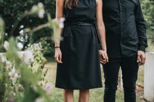 Man and woman wearing black, holding hands, and standing at a loved one's grave