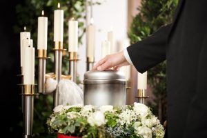 Silver urn at a memorial service, man lightly touching the lid in remembrance