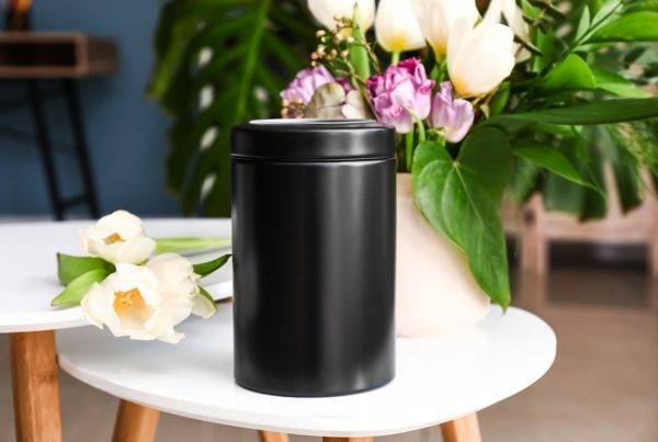 Black urn sitting on side table with flower vase nearby