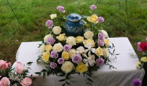 Urn sitting on memorial table surrounded by yellow and light purple flowers