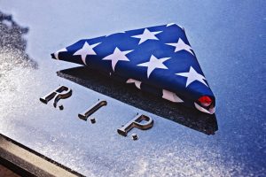 Folded American flag lying on top of a granite headstone that says R.I.P.