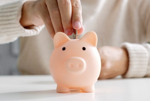 Person placing money into a light pink piggy bank