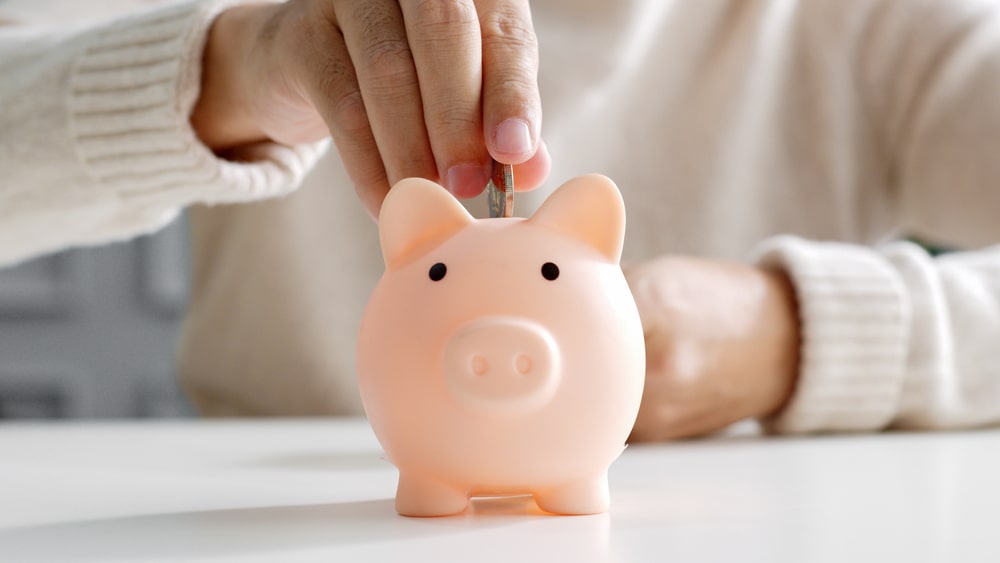 Person placing money into a light pink piggy bank