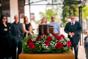 Dark colored urn surrounded by a ring of red roses with mourners in the background