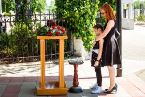 Mother and young daughter wearing black dresses, standing in front of urn, paying respects