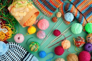 Yarn, knitting needles, and knitting projects laid out on a flat green surface