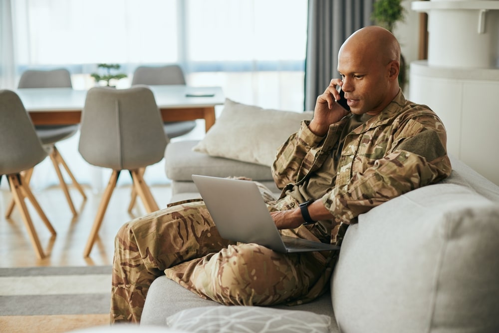 Man in uniform sitting on couch, talking on phone as he learns about veterans' burial benefits