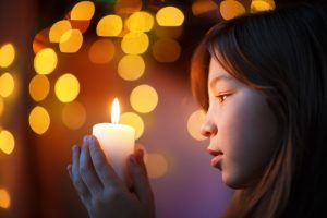 Young girl looking at lit candle she is holding in her hands