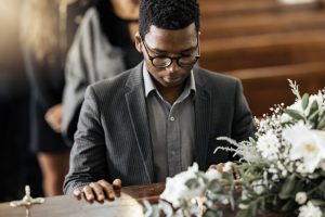 African American man placing his hand on a loved one's casket at a funeral