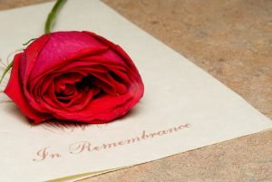 Funeral program with red rose resting on top of it