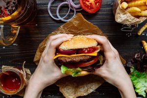 Hands holding a delicious burger with fries nearby