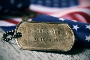 Weathered military dog tag that says "Thank you veterans" on it; American flag in the background