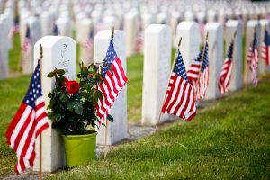 Government-issued headstones at a U.S. National Cemetery with American flags planted in the ground