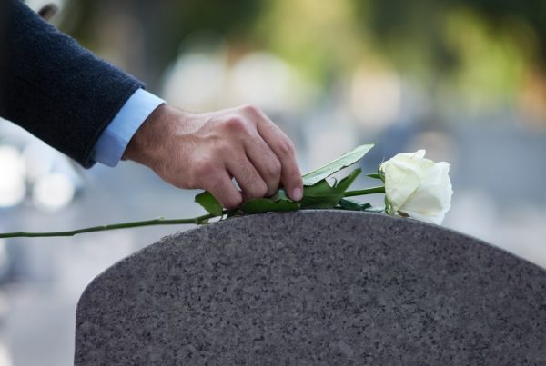 Man placing a white rose on top of a gravestone