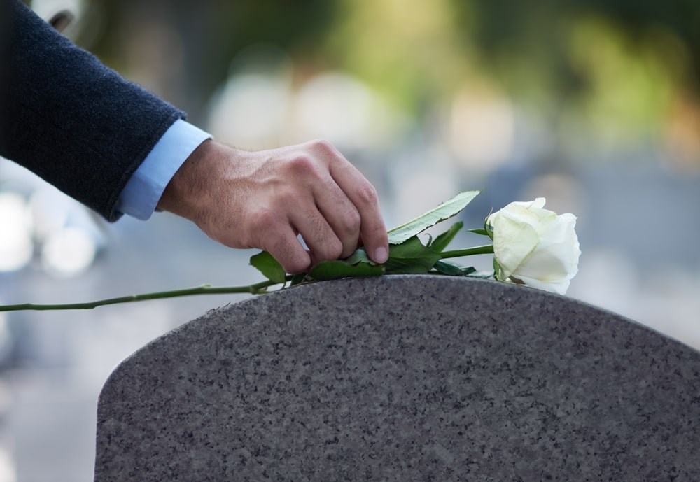 Man placing a white rose on top of a gravestone