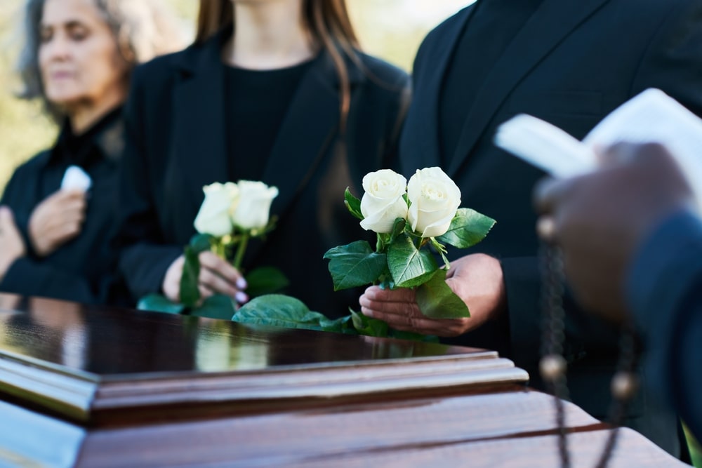 group of people placing white roses on a casket