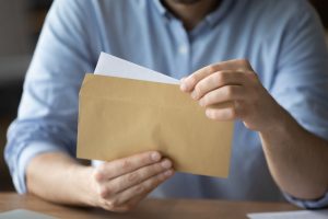 Man in blue button-down shirt opening a letter in a brown envelope