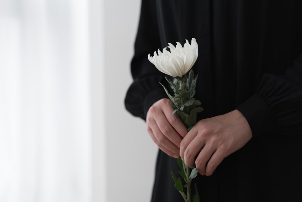Person wearing black coat and holding white memorial flower
