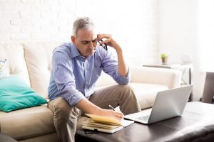 Man on a phone call, sitting on couch and writing in a notebook