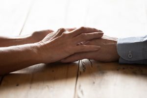 Two people sitting across from each other at table, touching hands, focus on hands