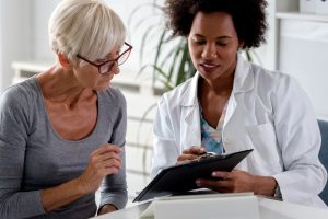 Mature woman sitting down with female doctor, reviewing paperwork together