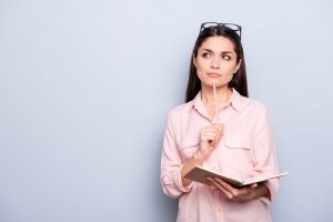 Woman holding a notebook and pen and thinking about goals