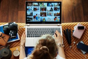 Woman sitting on couch and looking at photo library on her laptop; creating a memorial tribute video with technology