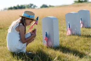 Sad, female child sitting in front of a military tombstone