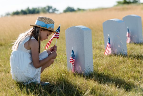 Sad, female child sitting in front of a military tombstone