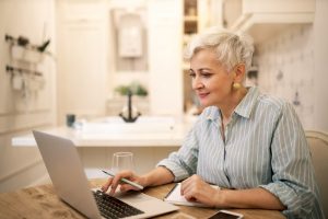 Mature woman sitting at home with a laptop in front of her, using an AI writer to assist her; using technology