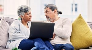 Man and wife sitting at home, talking as they look at a laptop; using technology to plan ahead for funeral