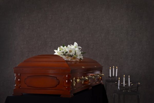 Casket with flowers on top next to rows of candles