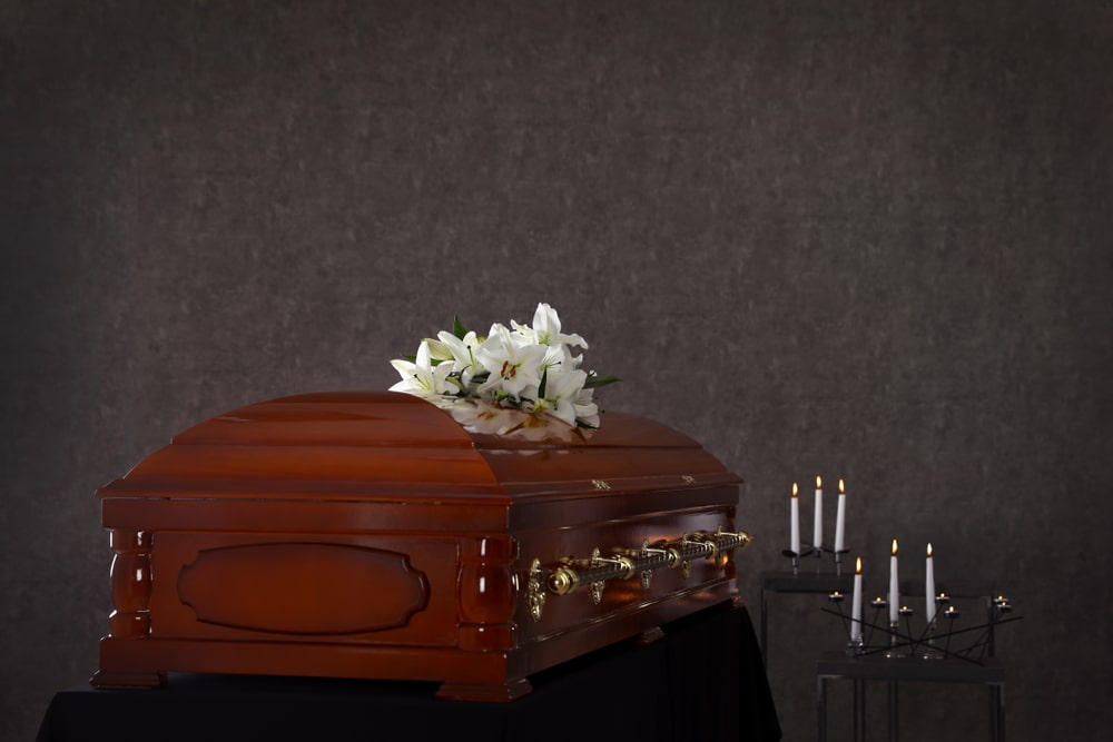 Casket with flowers on top next to rows of candles