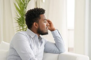 Young father sitting on a couch, looking out the window and thinking
