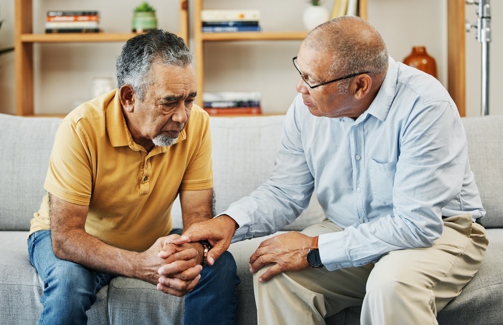 Two mature men sitting on a couch; one man counseling the other