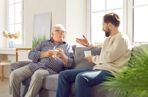 Father and son sitting on a couch in a bright room and talking