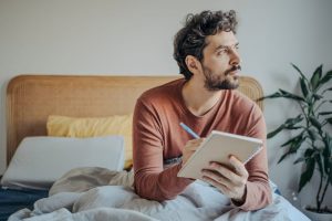 Man sitting in bed and writing in a journal