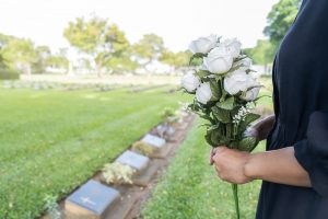 Woman in black dress holding white flower bouquet while visiting loved one's grave