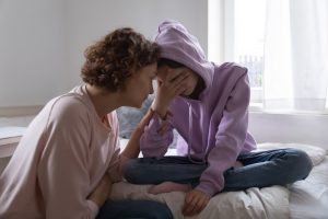 Mother and teenage daughter sitting together at home, upset over suicide loss