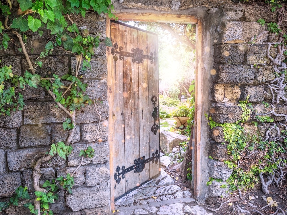 Door in an old, vine-covered wall opening into a beautiful garden