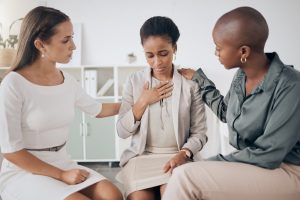 Three female co-workers sitting together, supporting the woman sitting in the middle