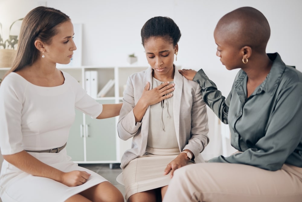 Three female co-workers sitting together, supporting the woman sitting in the middle