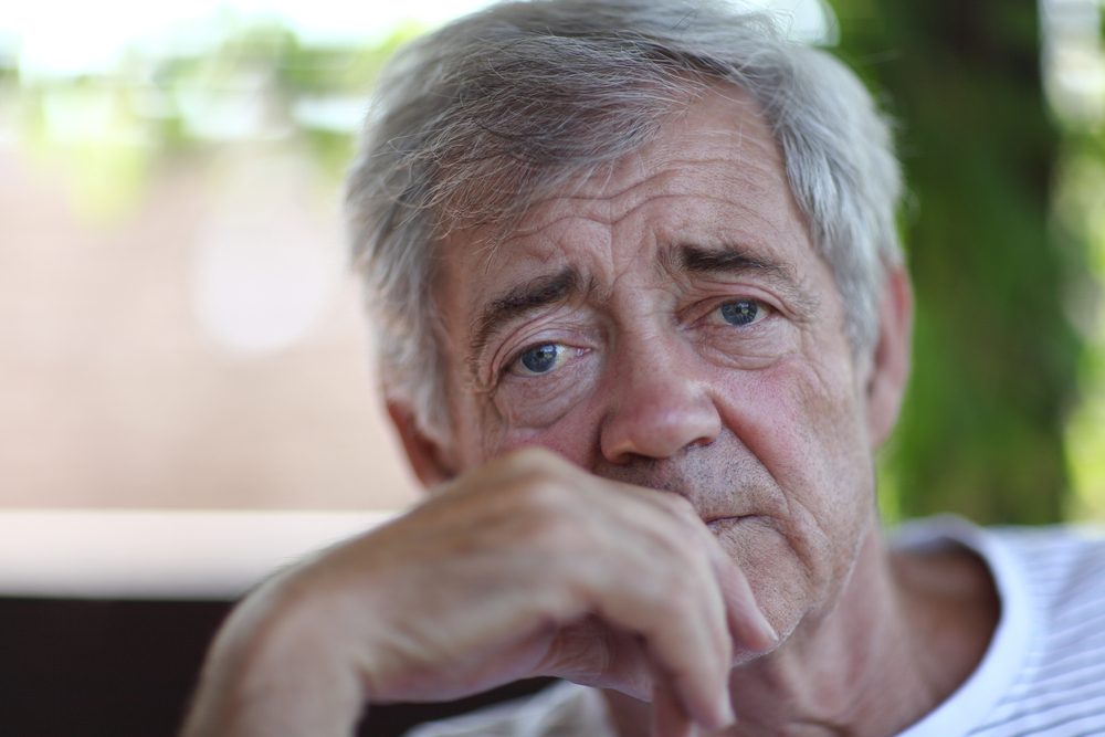 Older man, fingers to lips, staring toward camera, looking sad