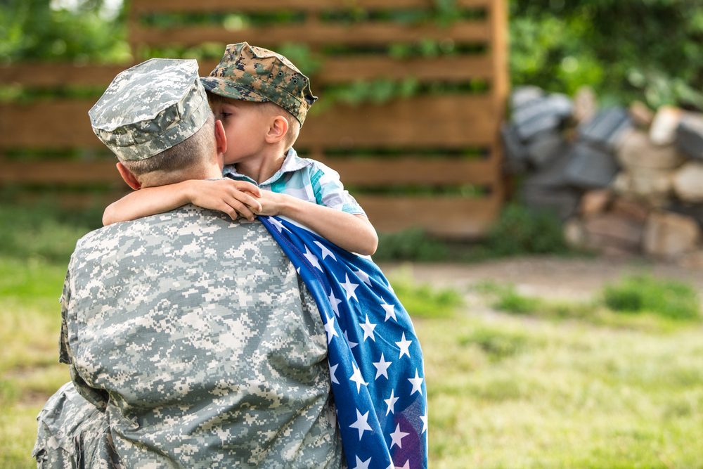 Young boy embracing his military father, American flag draped over father's shoulder