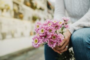 Person in white sweater leaving a flower memorial of pink flowers