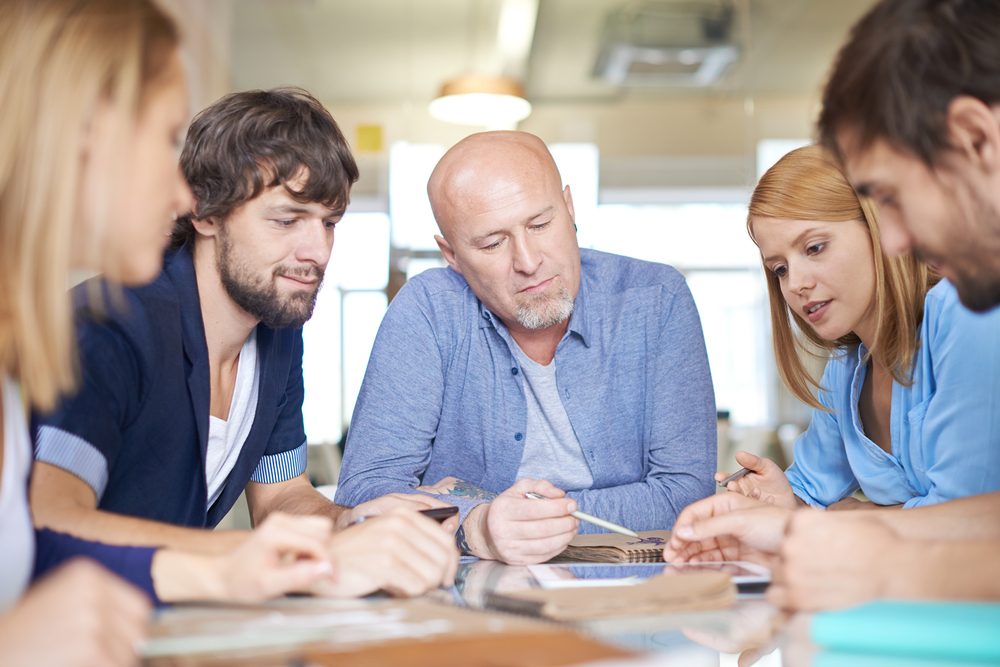 Group of five men and women sitting at a table, making plans